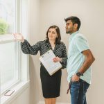 A real estate agent discusses property details with a client indoors, highlighting the view through large windows.